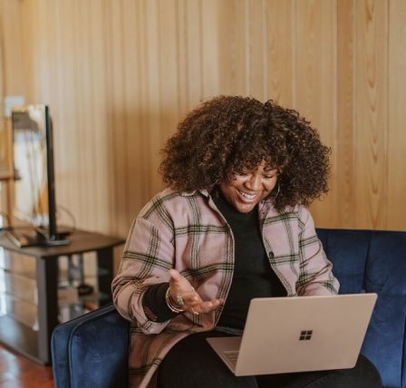 woman of colour sitting at a laptop on the sofa smiling at her laptop