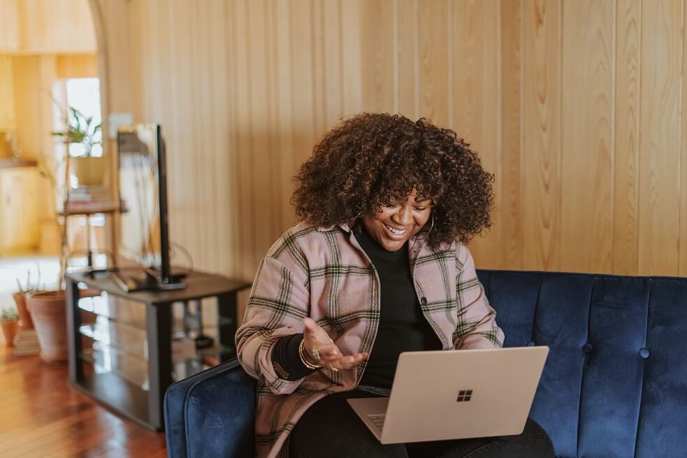 woman of colour sitting at a laptop on the sofa smiling at her laptop